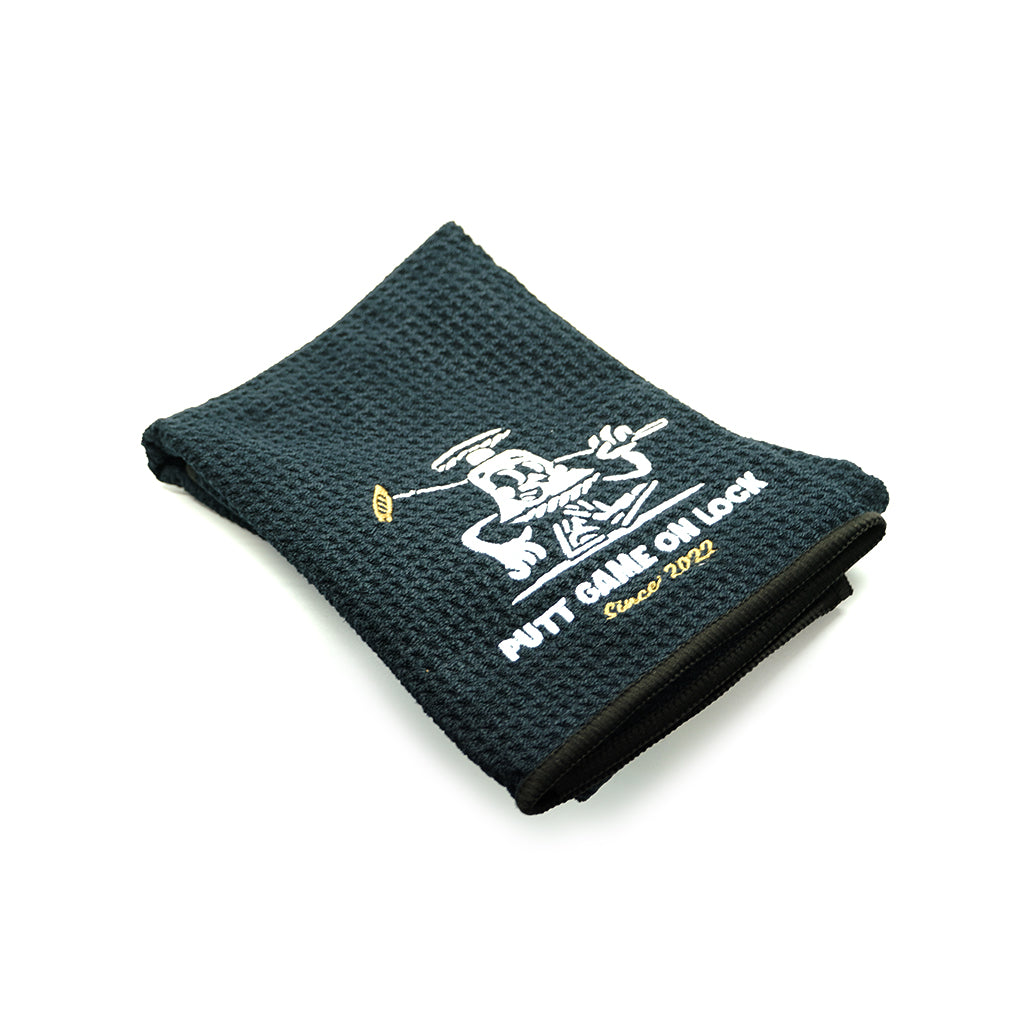 The official Last Golf Club x Leen Customs Golf Towel. Rectangular cotton terrycloth towel in black. Logo embroidered in white at face.  Made in Turkey.  Carabiner Clip Logo embroidered on front 40cm x 60cm