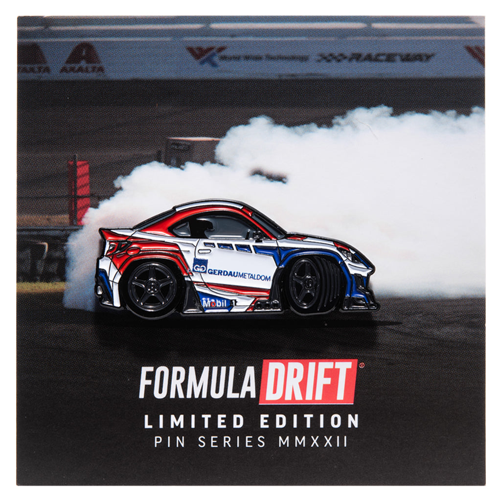 Metal enamel pin of drifter Jhonnattan Castro's FRS GR86. Colors: white, red, blue with black wheels. On backing card resembling a skid pad with smoke simulating a drift in motion.