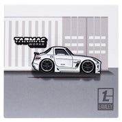 Metal enamel pin of a SLS AMG in white with black wheels with faded Lamley logo. In collaboration with the Lamley Group. On backing card resembling a shipping container with Lamley Group logo and Tarmac Works logo.