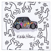 Metal enamel pin of a classic Mini with human figures dancing in Keith Haring style. Colors: white, orange, pink, blue, yellow. Equipped with silver Minilite wheels. On white backing card with dancing people, drawn in the Keith Haring art style, with Keith Haring logo.