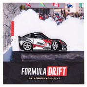 Metal enamel pin of a C6 Corvette with custom Formula D livery. Colors: white, red, grey with silver rear wheel and white front wheel. Front wheel is in full lock to simulate a drift in motion. On backing card resembling a fenced skid pad with smoke to emulate a drift in motion.