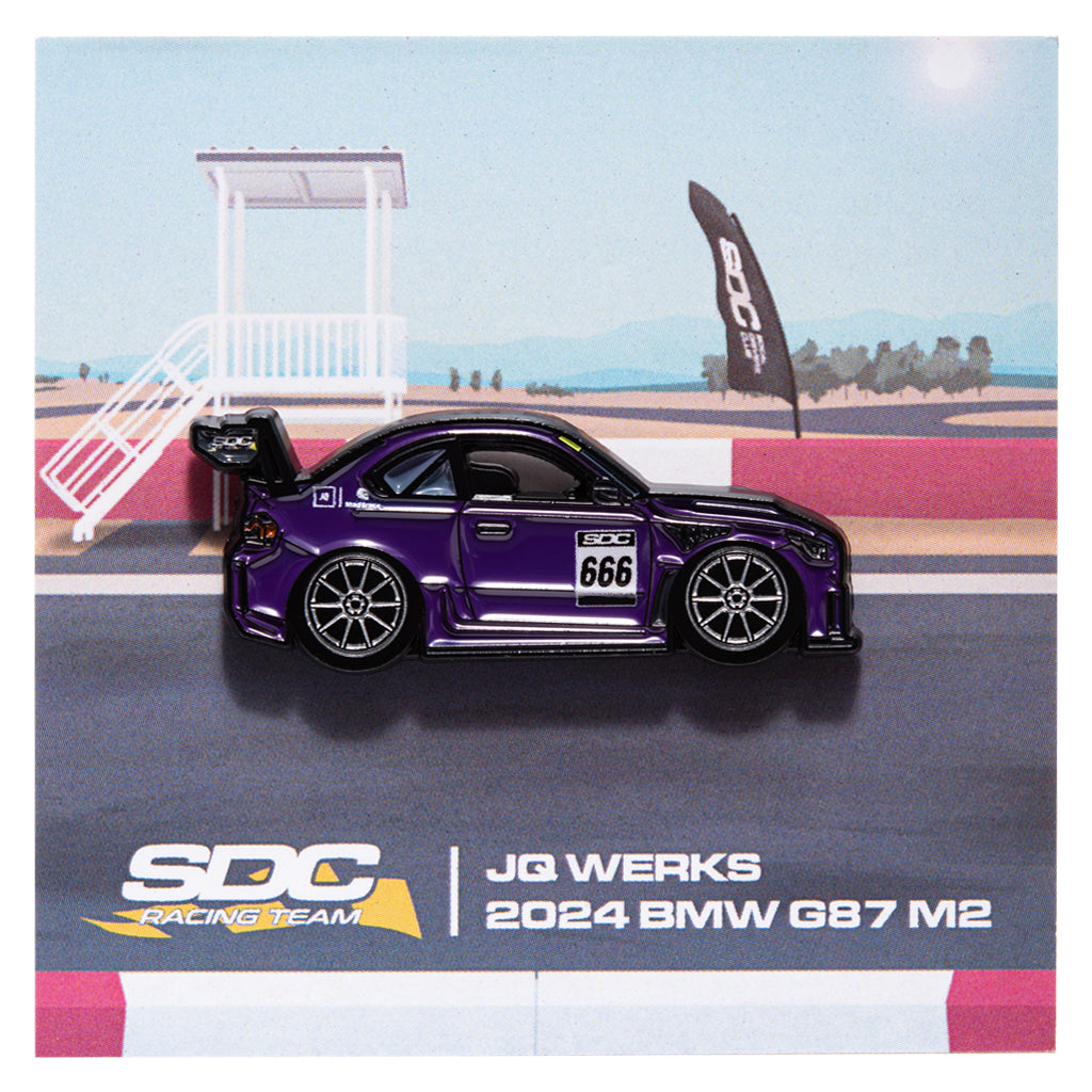 Purple BMW G87 M2 enamel pin on a racing track with SDC Racing Team branding